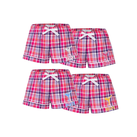 Four pairs of girls' plaid shorts arranged in a 2x2 grid on a white background. The shorts feature a pink, red, and blue plaid pattern with white drawstrings at the waist and various colorful 'SKATE' graphics on the left leg.