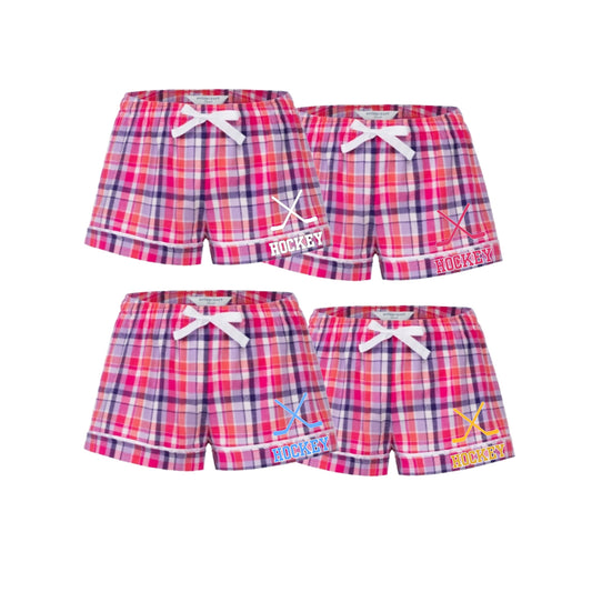 Pink Plaid shorts featuring a pink, red, and blue plaid pattern with white drawstrings and 'HOCKEY'' text and hockey sticks design.