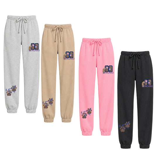 Jogger sweatpants in light gray, beige, pink, and black, each featuring a custom graphic patch on the thigh and a paw print graphic near the lower leg 'if you fall get up'.