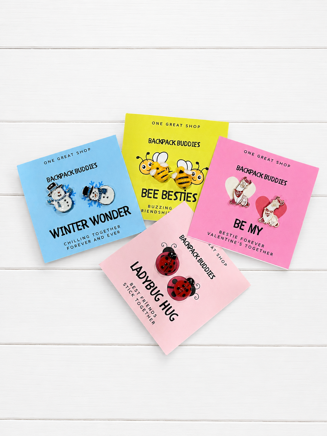 Four colorful backpack buddy cards. The cards feature different designs: blue 'Winter Wonder', yellow 'Bee Besties', pink 'Be My', and light pink 'Ladybug Hug', each with cute illustrations and the brand 'Backpack Buddies'.